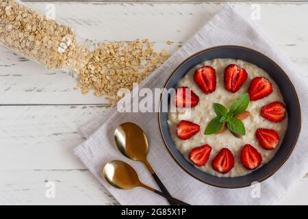 Haferbrei mit Erdbeerscheiben und Flocken in einer Schüssel auf dem weißen Tisch. Stockfoto