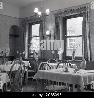 50er Jahre, historische, leere Tische in einem Café oder Teestuben der damaligen Zeit, mit Stoffdecken bedeckte Tische und Narzissen in Glasvasen, England. VEREINIGTES KÖNIGREICH. Stockfoto