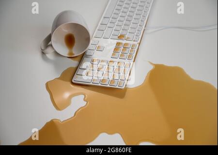 Verschüttete Tasse schwarzen Kaffee auf der Computertastatur auf dem weißen Tisch. Stockfoto