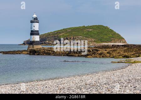 Der Kiesstrand am Penmon Point mit dem Leuchtturm und Puffin Island im Hintergrund, Anglesey, Nordwales Stockfoto