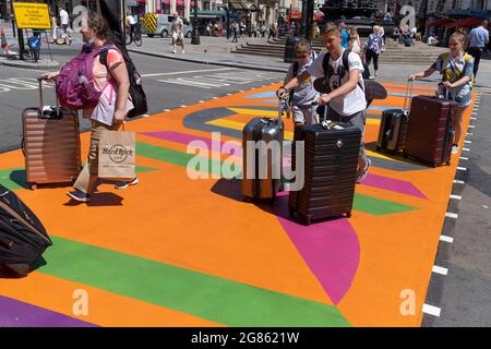 Eine Reisende Familie schiebt ihre Wheelie-Koffer am 16. Juli 2021 in London, England, über die mehrfarbigen Markierungen einer Kreuzung am Piccadilly Circus. Stockfoto