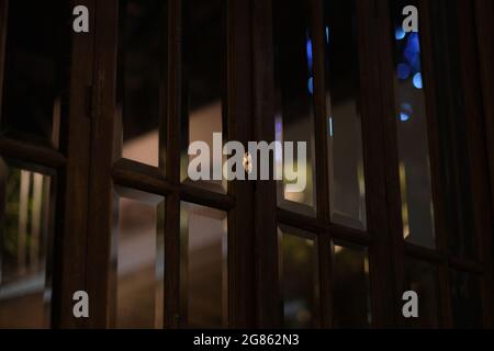Ein gut aussehendes altmodisches Fenster aus dickem Glas und dunklem Holz reflektiert die Straßenbeleuchtung während einer weiteren Sperrnacht in einem leeren Hotel in Pattaya Stockfoto