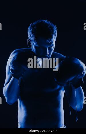 Kampfkunstkämpfer in Handschuhe in Neonblau. Männliches Porträt eines Boxers auf dunklem Hintergrund. Stockfoto