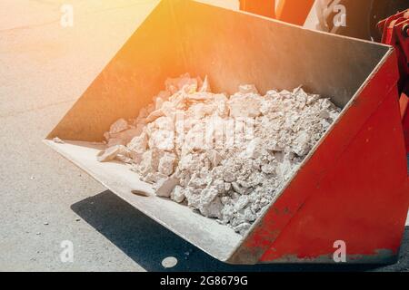 Entfernung von Bauschutt. Der Eimer des Traktors ist mit Betonschutt und Pflasterplatten gefüllt. Demontage des Straßenbelags. Stockfoto