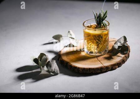 Gelber Cocktail auf dem Holzpodest Eukalyptus Rosmarin dunkel launisch Stockfoto