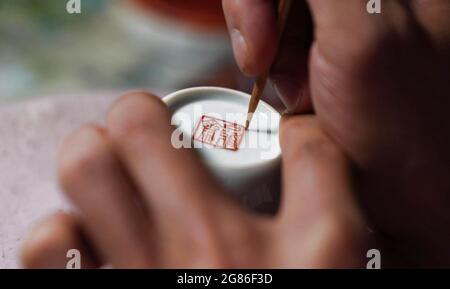 (210717) -- JINGDEZHEN, 17. Juli 2021 (Xinhua) -- Cheng Xiaoqian malt auf einen Guyacai-Porzellanbecher in einem Atelier in Jingdezhen, ostchinesische Provinz Jiangxi, 13. Juli 2021. Guyacai, wörtlich übersetzt malerische Farbdekoration auf Chinesisch, ist eine Art Porzellandekoration, die in den 1980er Jahren erfunden wurde. Seine Spezialität liegt in einer Kombination aus chinesischer Kunst und westlichen Gemälden. Ein Guyacai-Maler muss nicht nur gut über Pigmentmerkmale wissen, sondern auch geübte Fähigkeiten in westlicher und traditioneller chinesischer Malerei, Kalligraphie und Siegel beherrschen, um die Schönheit der klassischen und malerischen Kunst auszudrücken Stockfoto