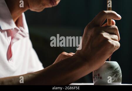 (210717) -- JINGDEZHEN, 17. Juli 2021 (Xinhua) -- Cheng Xiaoqian malt Guyacai auf einen Porzellanbecher in einem Atelier in Jingdezhen, ostchinesische Provinz Jiangxi, 13. Juli 2021. Guyacai, wörtlich übersetzt malerische Farbdekoration auf Chinesisch, ist eine Art Porzellandekoration, die in den 1980er Jahren erfunden wurde. Seine Spezialität liegt in einer Kombination aus chinesischer Kunst und westlichen Gemälden. Ein Guyacai-Maler muss nicht nur gut über Pigmentmerkmale wissen, sondern auch geübte Fähigkeiten in westlicher und traditioneller chinesischer Malerei, Kalligraphie und Siegel beherrschen, um die Schönheit der klassischen und malerischen Kunst auszudrücken Stockfoto