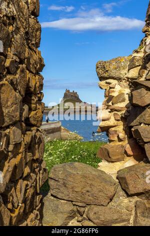 Ein Blick über den Hafen zum Schloss Lindisfarne auf Holy Island, Northumberland, durch eine Lücke in den alten Ruinen der Festung. Stockfoto