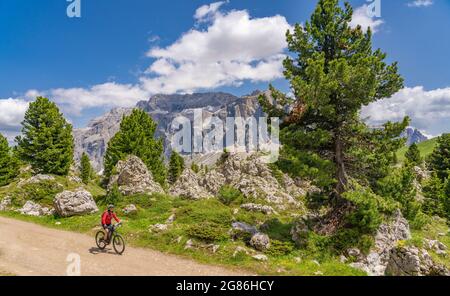 Aktive ältere Frau auf ihrem Elektro-Mountainbike berühmte Steinstadt unter dem Langkofel-Gipfel in den Sella-Dolomiten von Wolkenstein, Südtirol Stockfoto