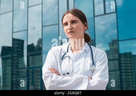 Junge Ärztin, die vor dem Krankenhaus steht. Nahaufnahme. Stockfoto