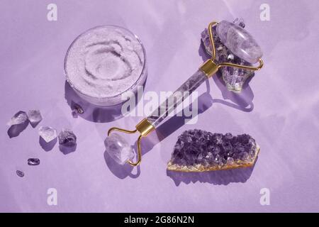 Amethyst Kristalle Gua Sha Roller Massage Scraper und Beauty-Produkt. Feuchtigkeitscreme und Hautpflegemittel. Wellness-Konzept. Stockfoto
