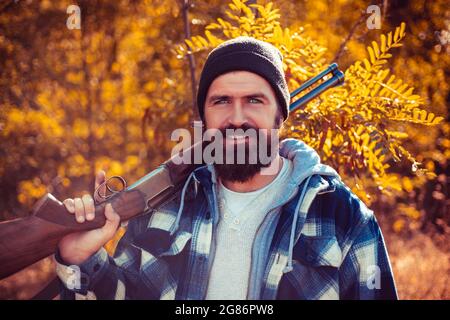 Bärtiger Jäger mit Waffe und Spaziergang im Wald. Jäger mit Schrotflinte auf der Jagd. Herbstjagd. Stockfoto