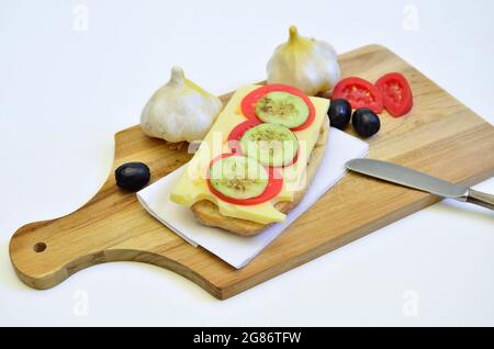 Käsesandwich mit Tomaten, Gurke, Knoblauch und schwarzen Oliven auf Schneidebrett, Nahaufnahme, isoliert auf weißem Hintergrund Stockfoto