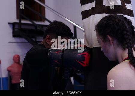 Junge spanische Trainerin mit Boxsack für professionelle lateinamerikanische Boxerin Stockfoto