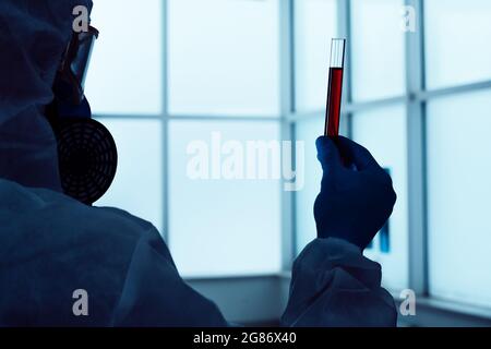 Bild eines Wissenschaftlers in voller Schutzausrüstung mit einem Reagenzglas in den Händen. Stockfoto