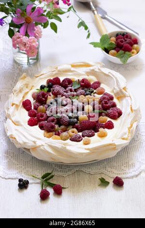 Pavlova-Kuchen mit Creme und Beeren und einem Blumenstrauß auf hellem Hintergrund. Stockfoto