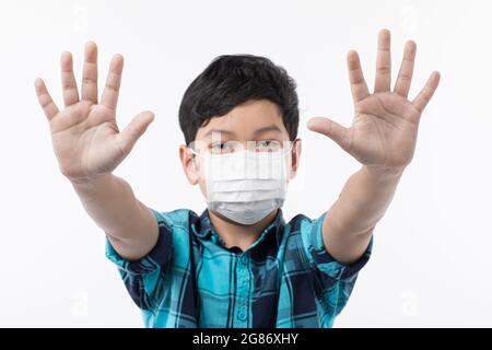 Youn niedlichen kleinen asiatischen Jungen trägt chirurgische Hygiene-Schutzmaske auf weißem Hintergrund steigt Hand im Zeichen von Abfall, zu verhindern, zu stoppen und Nein zu den Stockfoto