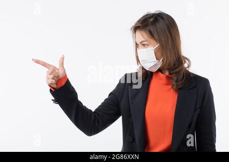 ฺBusiness Frau in schwarzem Anzug trägt chirurgische schützende Hygienemaske auf Gesicht zeigen Finger irgendwo leer. Idee zur Vorbeugung von Gesundheit vor Viren Stockfoto