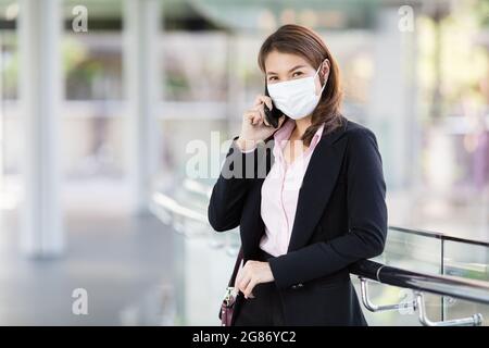 Schöne nette lächelnde asiatische Geschäftsfrau trägt schützende chirurgische Hygienemaske auf dem Gesicht in der Situation des Coronavirus Ausbruch, im Geschäft stehend Stockfoto