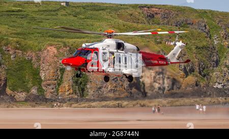 Lunan Bay Beach, Angus, Schottland, Großbritannien, 17. Juli 2021: Große Rettungsaktion der Küstenwache und RNLI, nachdem eine Mutter und Tochter heute am Lunan Bay Beach mit ihrem aufblasbaren Schlauchboot bei starkem Wind auf See getrieben wurden. Ein Offshore-Versorgungsschiff, das sich in der Nähe befand, startete ebenfalls seinen FRC, um bei der Rettung zu helfen. Auf diesem Foto können Sie den Küstenwache-Hubschrauber sehen, der am Strand an Land kommt, während einer der Hubschrauber-Crew aus der Tür schaut und Mitglieder der Öffentlichkeit darauf blicken. (Quelle: Barry Nixon/Alamy Live News) Stockfoto