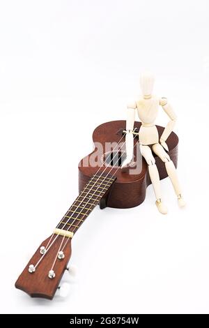 Ukulele Akustikgitarre mit menschlichen Schaufensterpuppe Figur. Pause für Hobby. Kunst oder musikalisches Konzept. Braune hawaii-Gitarre und Holzpuppe Stockfoto