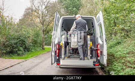 Einer behinderten Person im Rollstuhl wurde geholfen, in einen speziell angepassten Schulbus zu gelangen. Stockfoto