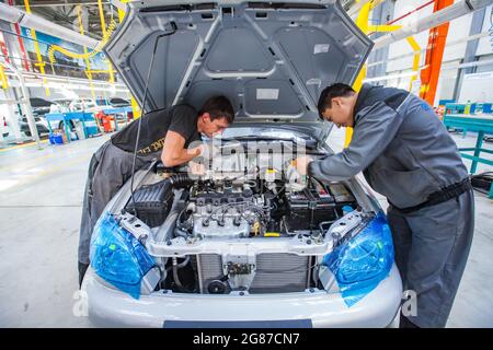 Kostanay, Kasachstan, 14.Mai2012: Automatische Montageanlage für Saryarkaavtoprom-Gebäude. Ssangyong Cars Förderlinie. Junge asiatische Arbeiter installieren Triebwerke Stockfoto