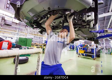 USt'-Kamenogorsk, Kasachstan, Mai 31,2012:Auto-Gebäude-Fabrik der Asia-Auto-Firma. Junger asiatischer Arbeiter installiert Motorteile unten im Auto. Innenraum der Werkstatt. Stockfoto