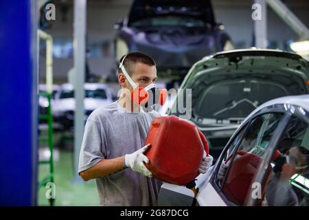 USt'-Kamenogorsk, Kasachstan-Mai 31,2012:Auto-Gebäude der Asia-Auto-Firma. Junger Arbeiter in Atemschutzmasken, die das Auto mit Benzin (Kraftstoff) von jerry Can befüllen. Stockfoto