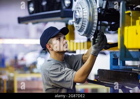 USt'-Kamenogorsk, Kasachstan - Mai 31,2012: Auto-Gebäude der Firma Asia-Auto. Junger kaukasischer Arbeiter, der Autoaufhängung und Radnabe montiert. Stockfoto