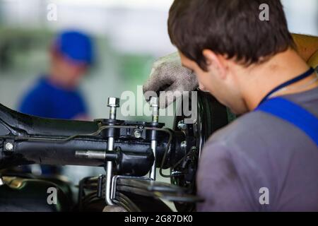 Region Almaty, Kasachstan, 06. Juni 2012:Werk der Firma Astana-Motors.Montage von Hyundai-Bussen.Arbeiter in schmutzigen Baumwollhandschuhen, Schrauben in der Aufhängung. Stockfoto