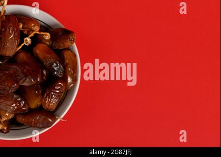 Zugeschnittenes Bild eines Tellers mit köstlichen frischen Datteln. Roter Hintergrund, Kopierbereich. Leckeres Essen zum Fastenbrechen im Ramadan Stockfoto