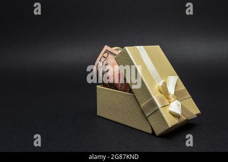 Geld als Geschenk. Ein Dollarschein in einer Kiste mit einem Bogen, auf einem schwarzen homogenen Hintergrund. Ort für Ihren Text. Stockfoto