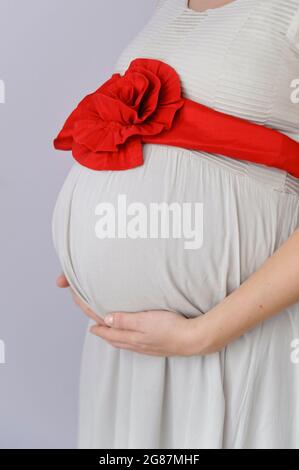 Schöne Nahaufnahme eines schwangeren Bäuches, sanft von liebevollen Händen gewiegt, symbolisiert die Verbindung zwischen Mutter und Baby. Die warme Beleuchtung und der weiche Fokus Stockfoto