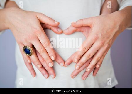 Schöne Nahaufnahme eines schwangeren Bäuches, sanft von liebevollen Händen gewiegt, symbolisiert die Verbindung zwischen Mutter und Baby. Die warme Beleuchtung und der weiche Fokus Stockfoto