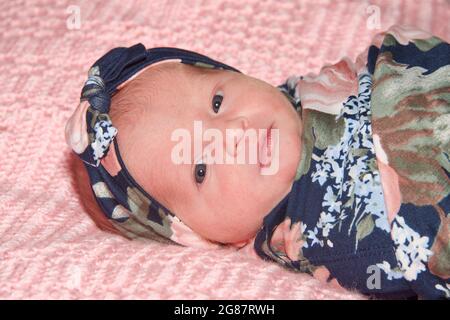 Nahaufnahme Porträt eines neugeborenen Mädchens mit braunen Haaren trägt geblümten Stirnband in Decke des gleichen Musters gewickelt Blick auf den Betrachter. Auf einem liegen Stockfoto