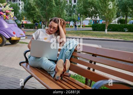 Rotschopf Mädchen auf einer Bank auf einem Laptop arbeiten Stockfoto