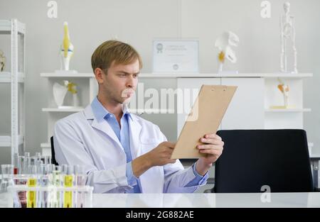 Der junge brasilianische Wissenschaftler las die Ergebnisse der Forschung an chemischen Verbindungen in der Zwischenablage. Arbeitsatmosphäre im chemischen Labor. Reagenzgläser fillen Stockfoto