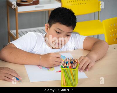 Das behinderte Kind im Rollstuhl lernt im Laufe der Entwicklungsübungen zu Hause über Zeichnen und Malen. Bildung und besonderes Kind Stockfoto