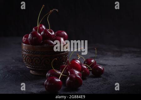 Bio-Kirsche in einer Schüssel mit Wassertropfen auf Beeren auf dunklem Grund. Nahaufnahme, Low-Key. Stockfoto