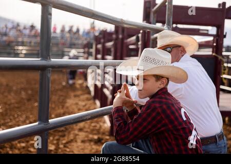 Bloomington, Usa. Juli 2021. Ein Junge beobachtet, wie ein Ansager vor dem Bar J Rodeo 3 auf der Monroe County Fair Einführungen gibt. Die Monroe County Fair in Bloomington, Indiana, ist eine einwöchige Ausstellung für Kunsthandwerk, landwirtschaftliche Produkte und Viehzucht, ein Gemeindetreffen und ein Festival, das auf dem County Fairgrounds stattfindet. County Messen in den USA sind eine Tradition und Teil der Kultur tief in ländlichen amerikanischen Leben verwurzelt. County Messen begann vor langer Zeit als eine Möglichkeit für Landwirte und landwirtschaftliche Arbeitnehmer zu sammeln und Kontakte zu knüpfen. Kredit: SOPA Images Limited/Alamy Live Nachrichten Stockfoto