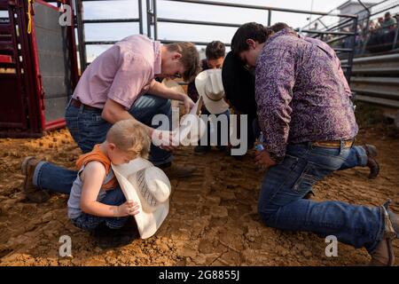 Bloomington, Usa. Juli 2021. Ein Junge betet mit einer Gruppe von Rodeo-Teilnehmern vor dem 3 Bar J Rodeo auf der Monroe County Fair. Die Monroe County Fair in Bloomington, Indiana, ist eine einwöchige Ausstellung für Kunsthandwerk, landwirtschaftliche Produkte und Viehzucht, ein Gemeindetreffen und ein Festival, das auf dem County Fairgrounds stattfindet. County Messen in den USA sind eine Tradition und Teil der Kultur tief in ländlichen amerikanischen Leben verwurzelt. County Messen begann vor langer Zeit als eine Möglichkeit für Landwirte und landwirtschaftliche Arbeitnehmer zu sammeln und Kontakte zu knüpfen. Kredit: SOPA Images Limited/Alamy Live Nachrichten Stockfoto