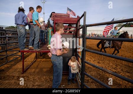 Ein Junge hört mit einer Gruppe von Rodeo-Teilnehmern vor dem 3 Bar J Rodeo auf der Monroe County Fair das Spielen der Nationalhymne. Die Monroe County Fair in Bloomington, Indiana, ist eine einwöchige Ausstellung für Kunsthandwerk, landwirtschaftliche Produkte und Viehzucht, ein Gemeindetreffen und ein Festival, das auf dem County Fairgrounds stattfindet. County Messen in den USA sind eine Tradition und Teil der Kultur tief in ländlichen amerikanischen Leben verwurzelt. County Messen begann vor langer Zeit als eine Möglichkeit für Landwirte und landwirtschaftliche Arbeitnehmer zu sammeln und Kontakte zu knüpfen. Stockfoto