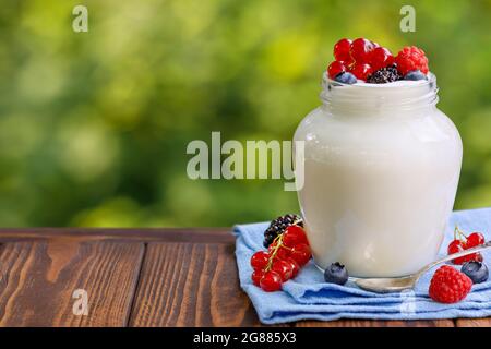 Joghurt mit frischen Beeren im Glas auf Holztisch im Freien Stockfoto