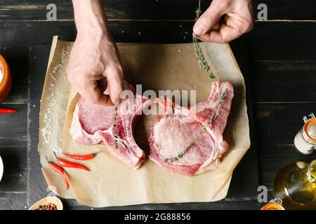 Mann, der rohes Schweinefleisch auf einem dunklen Holztisch zubereitet Stockfoto