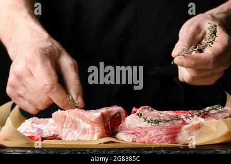 Mann, der rohes Schweinefleisch auf einem dunklen Holztisch zubereitet, Nahaufnahme Stockfoto