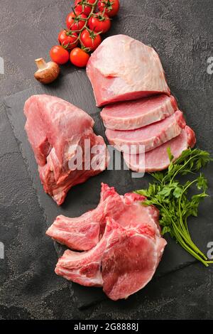 Scheiben rohes Schweinefleisch, Petersilie, Pilz und Tomate auf dunklem Hintergrund Stockfoto