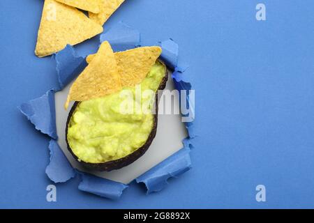 Kreative Komposition mit leckerer Guacamole in Avocado-Schale und Nachos auf farbigem Hintergrund Stockfoto