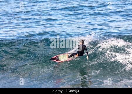 Australischer Mann im Neoprenanzug auf seinem Surfbrett, der an einem Wintertag an einem Strand in Sydney, NSW, Australien, die Wellen surft Stockfoto