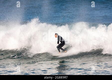 Australischer Mann im Neoprenanzug, der an einem Wintertag in Australien auf seinem Surfbrett im Avalon Beach Sydney die Wellen surft Stockfoto